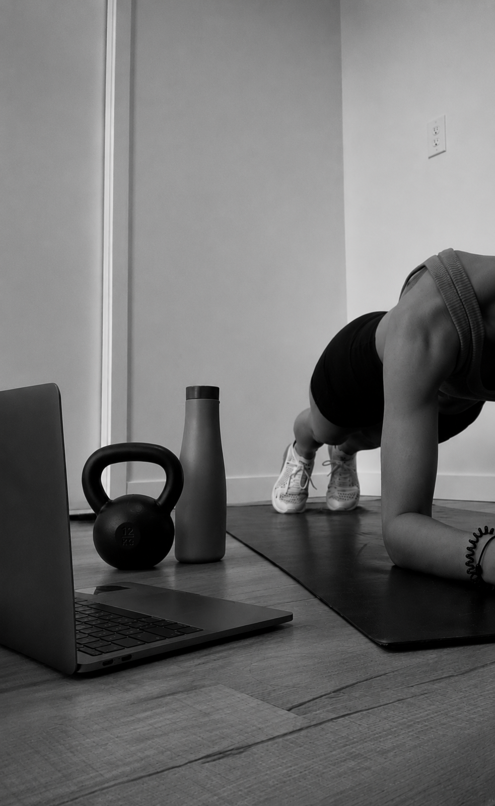 Person doing a home plank workout beside a laptop, kettlebell, and water bottle for the online Forge40 programme.
